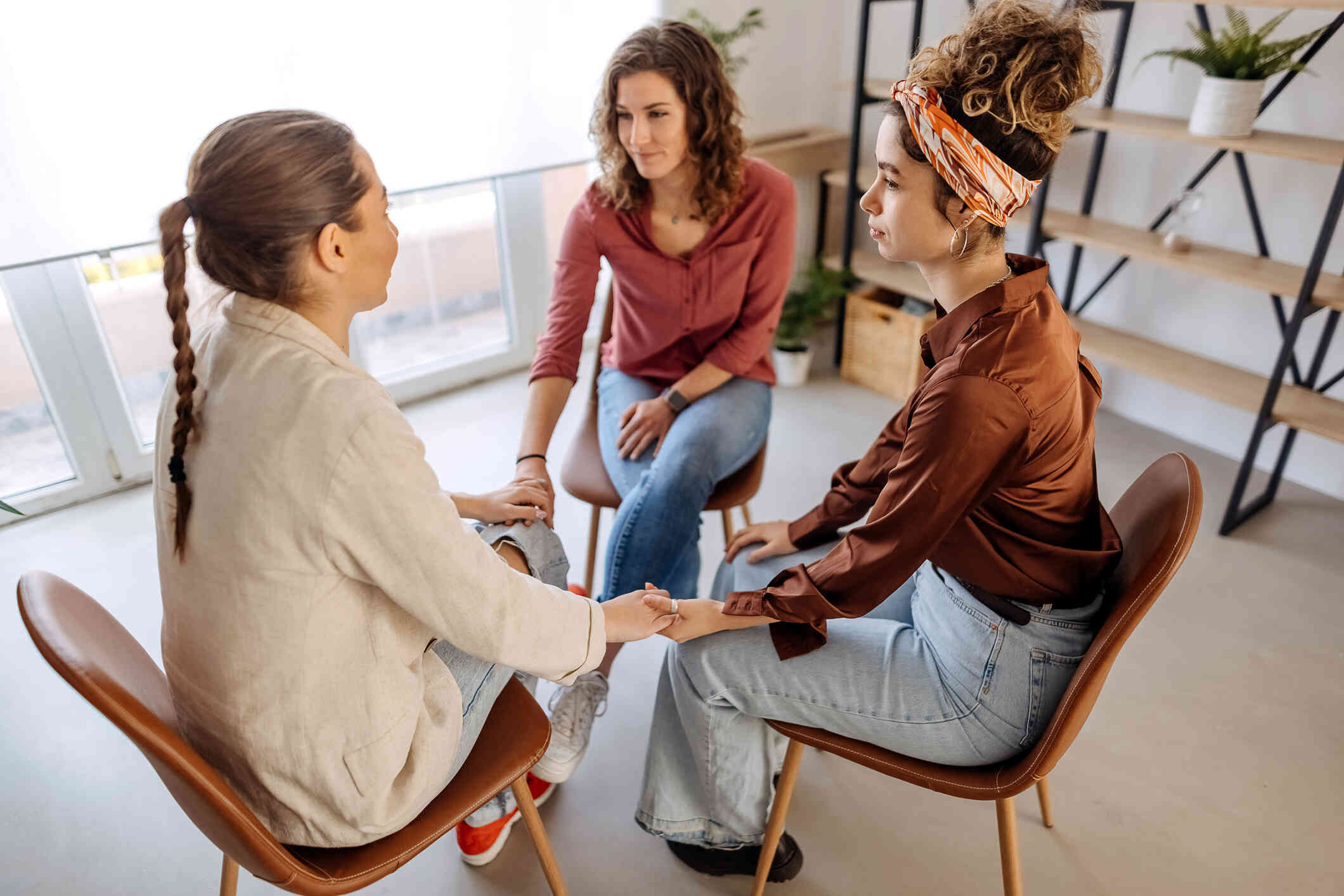 Three women are seated in a circle of chairs, engaged in what appears to be a therapy or group discussion session.